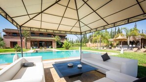 A covered outdoor seating area with white sofas and a pool in the background. - Exclusive luxury villa (Marrakesh)