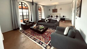 A spacious living room with a large sofa, a coffee table, and a patterned rug. There is a dining area with a table and chairs in the background. - Exclusive luxury villa (Marrakesh)