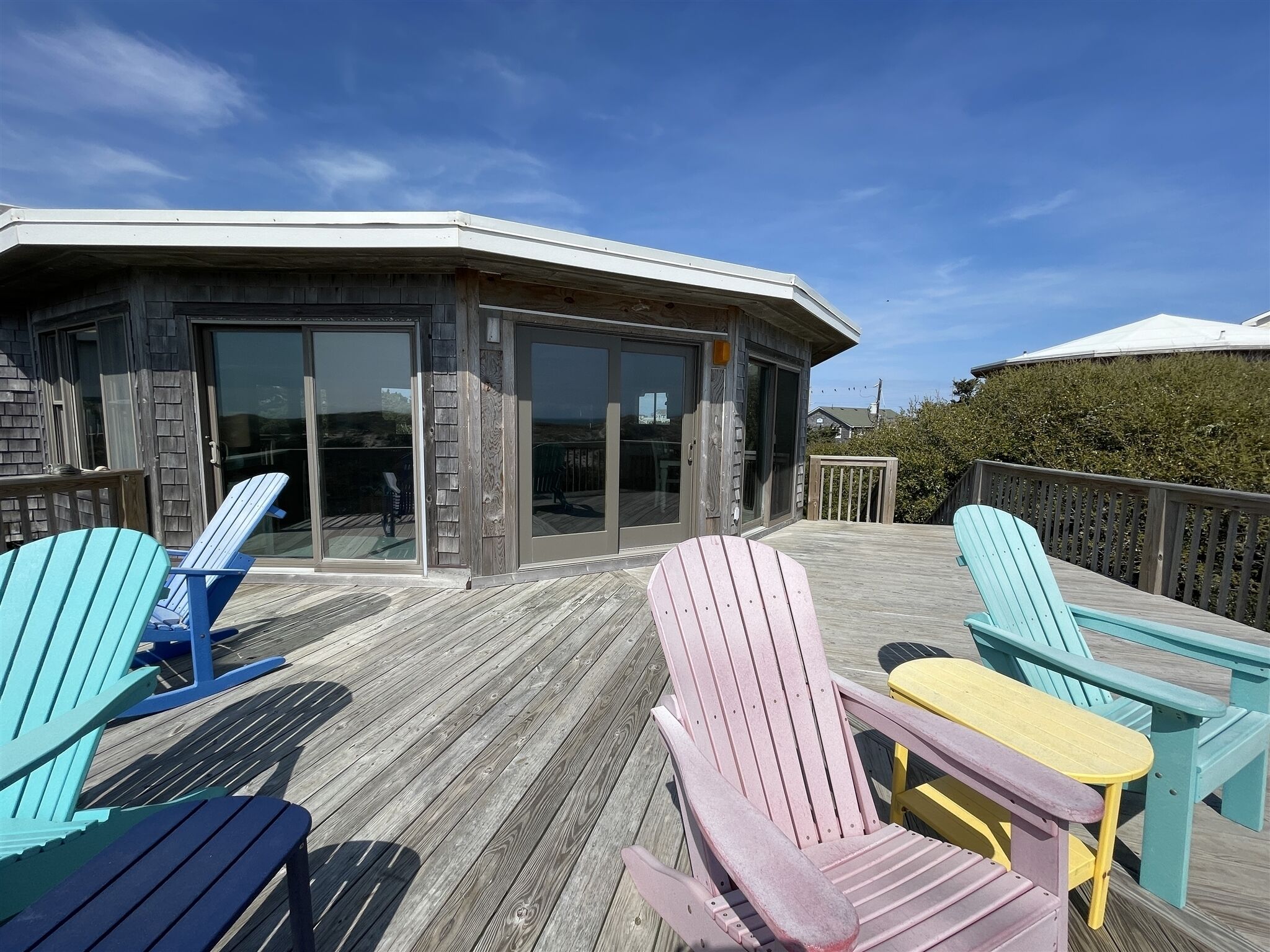 A wooden deck with Adirondack chairs and a covered area with glass doors.