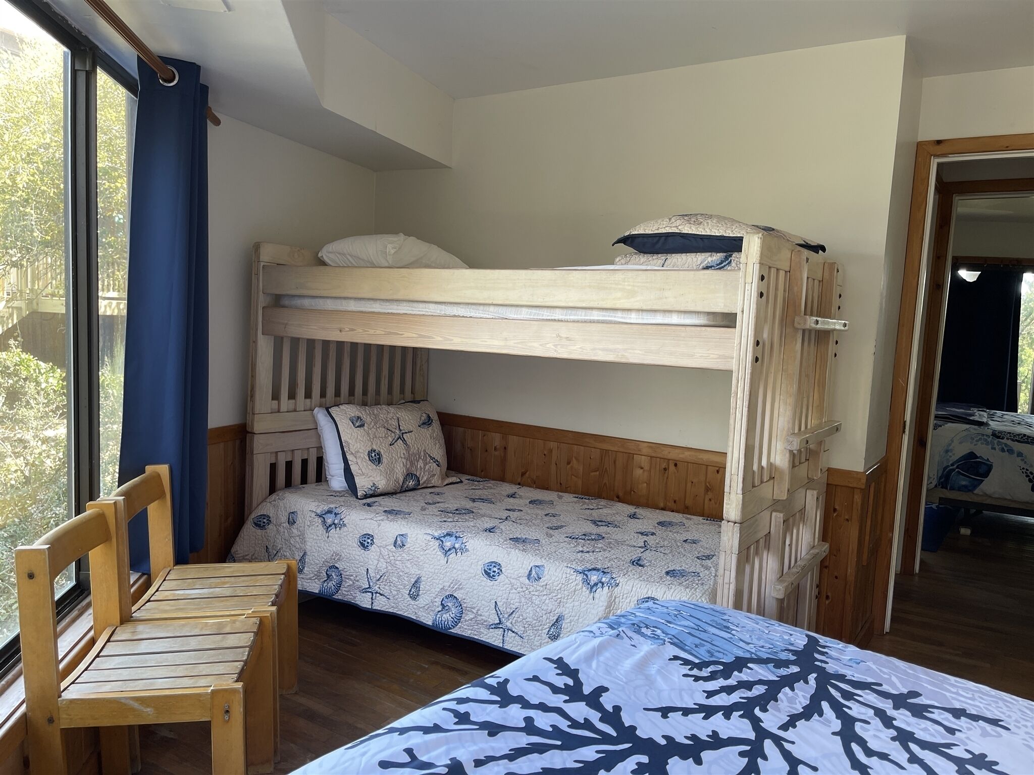 A bunk bed with a wooden headboard, a matching bench, and a patterned bedspread.