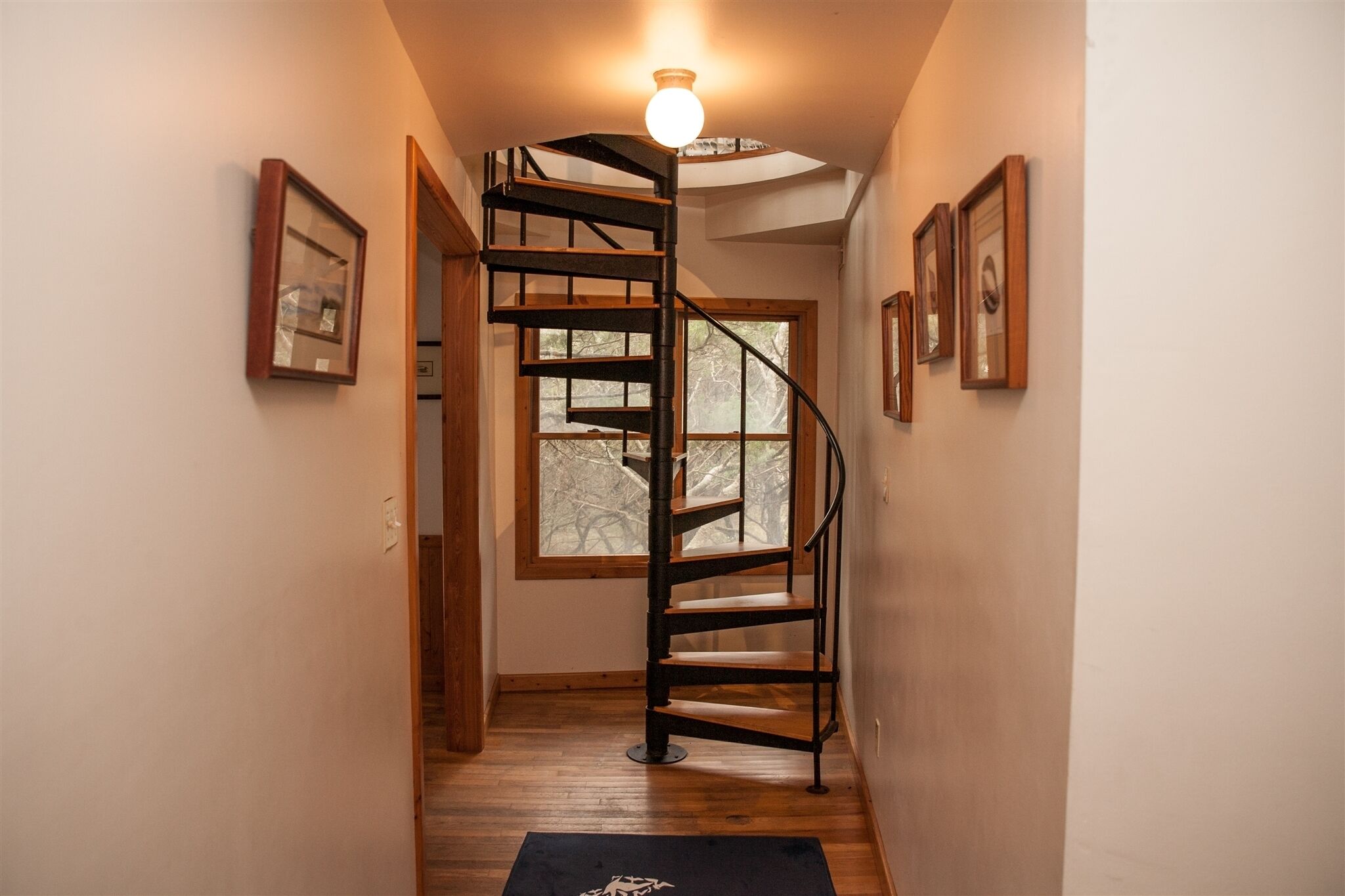 Una escalera en espiral de madera con una lámpara arriba, que lleva a una habitación con un ventanal.