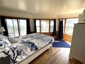 Une chambre à coucher avec un lit, un plancher en bois, de grandes fenêtres et une vue sur les arbres.