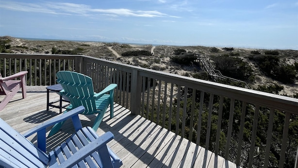 Eine Holzterrasse mit Stühlen mit Blick auf einen Strand.