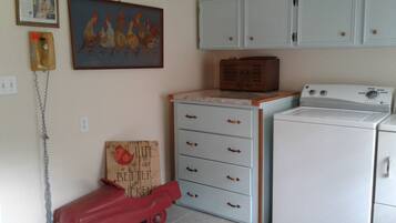 Un cuarto de lavado con una lavadora antigua, un camión de juguete rojo y un cuadro de gallinas en la pared.