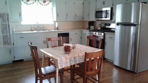 A kitchen with wooden cabinets, a stainless steel refrigerator, a microwave, and a dining table with chairs. - Comfort and Chickens (Clarksville)