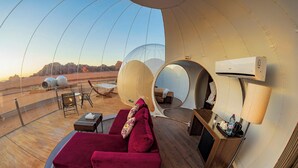 Eine luxuriöse Zelthütte mit einer bequemen roten Couch, einem kleinen Tisch und einem Stuhl. Ein großer Spiegel spiegelt das Innere wider, und eine Klimaanlage ist an der Zeltwand montiert.
