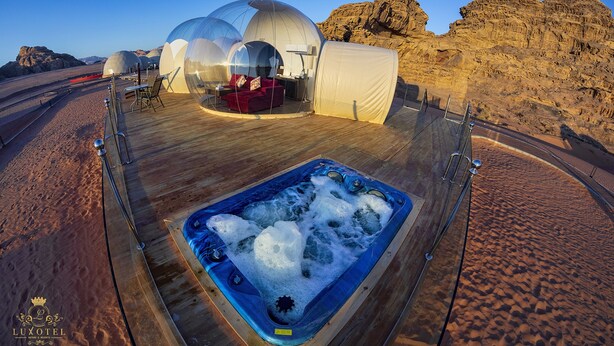 Ein Wüstenresort mit Unterkünften in transparenten Kuppeln, einer Holzterrasse und einem Whirlpool.