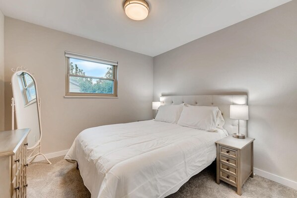 A bedroom with a bed, bedside tables, a dresser, a mirror, and a window.
