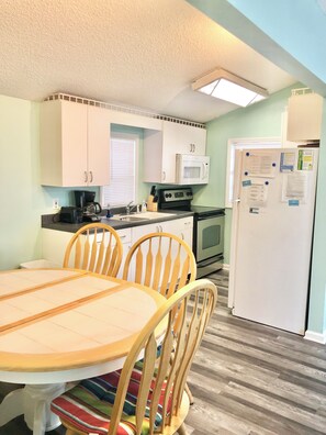 A compact kitchen with white cabinets, a microwave, a stove, and a refrigerator. There is a dining table with chairs and a striped rug. - Close to beach, Pet friendly, Golf cart (Myrtle Beach)