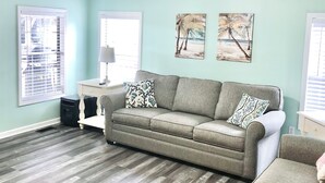 A living room with a grey sofa, a white side table, and two paintings on the wall.