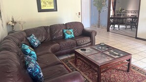 A living room with a brown leather sofa, a glass-top coffee table, and a patterned rug.