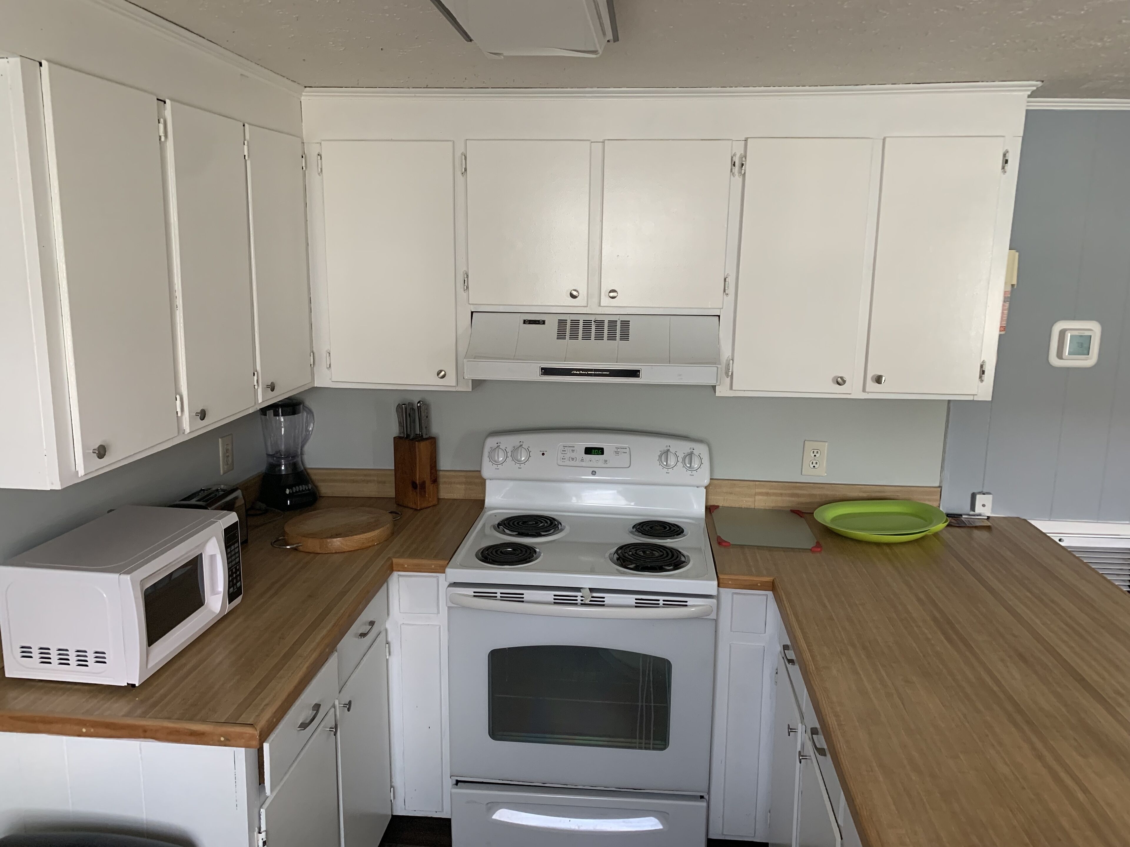 Une cuisine de taille réduite avec des meubles blancs, une cuisinière blanche et un four à micro-ondes.