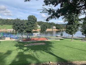 Un parque con un área de juegos, un lago y una casa al fondo.
