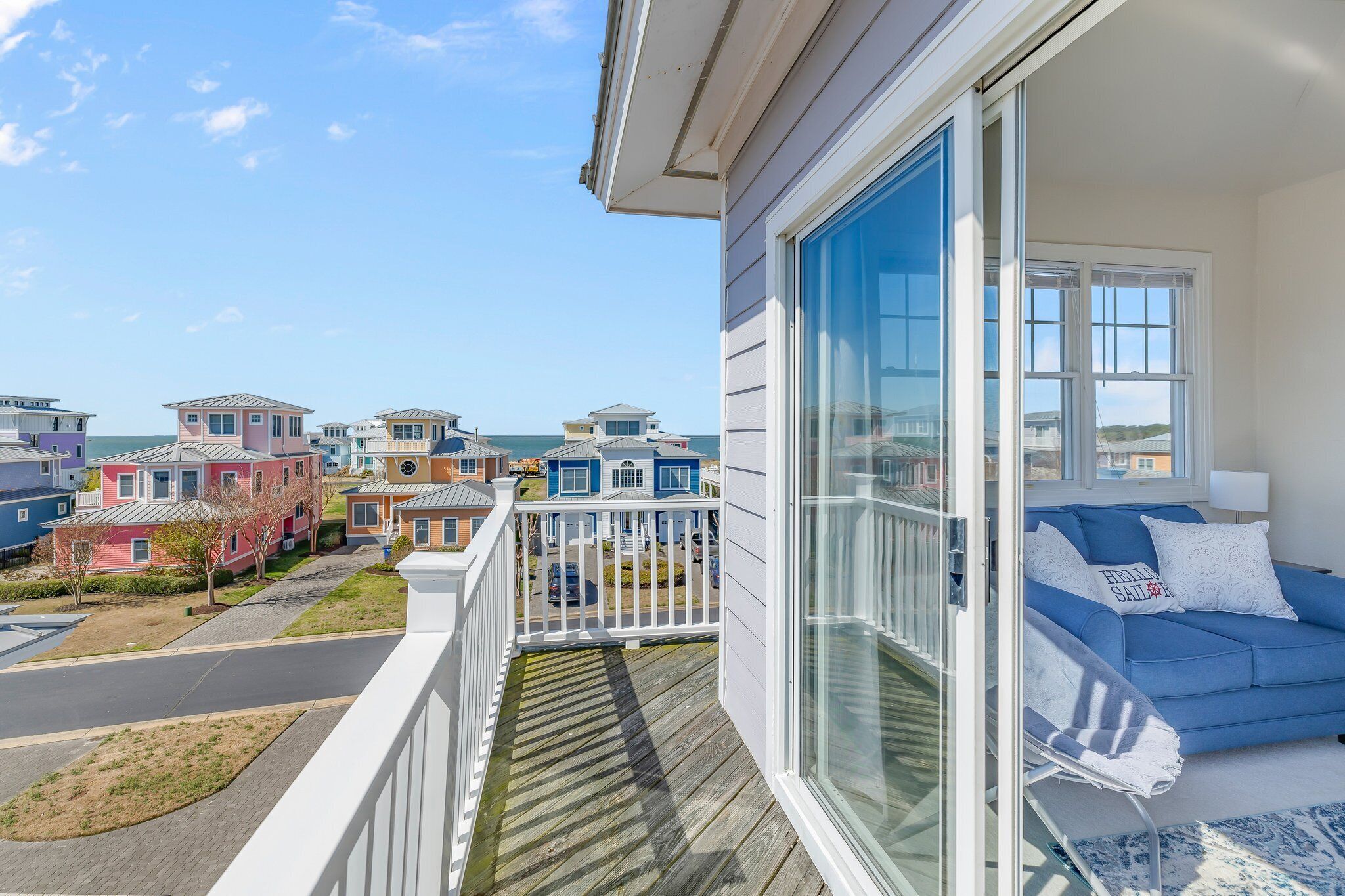 A balcony with a view of neighboring houses, a blue sofa with pillows, and a white railing.
