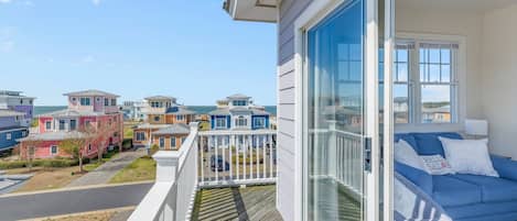 Varanda com vista para casas vizinhas, um sofá azul com almofadas e um corrimão branco.