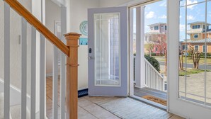 A hallway with a wooden staircase, a door leading outside, and a view of neighboring houses. - Only 1 Block to the Beach - Community Pool - Featured on HGTV!  (Cape Charles)