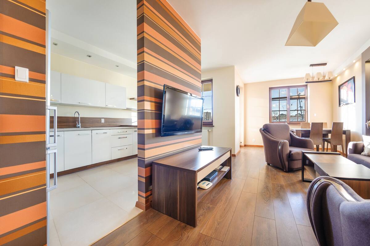 Una cocina moderna con gabinetes blancos, un televisor integrado y una mesa de comedor de madera con sillas.