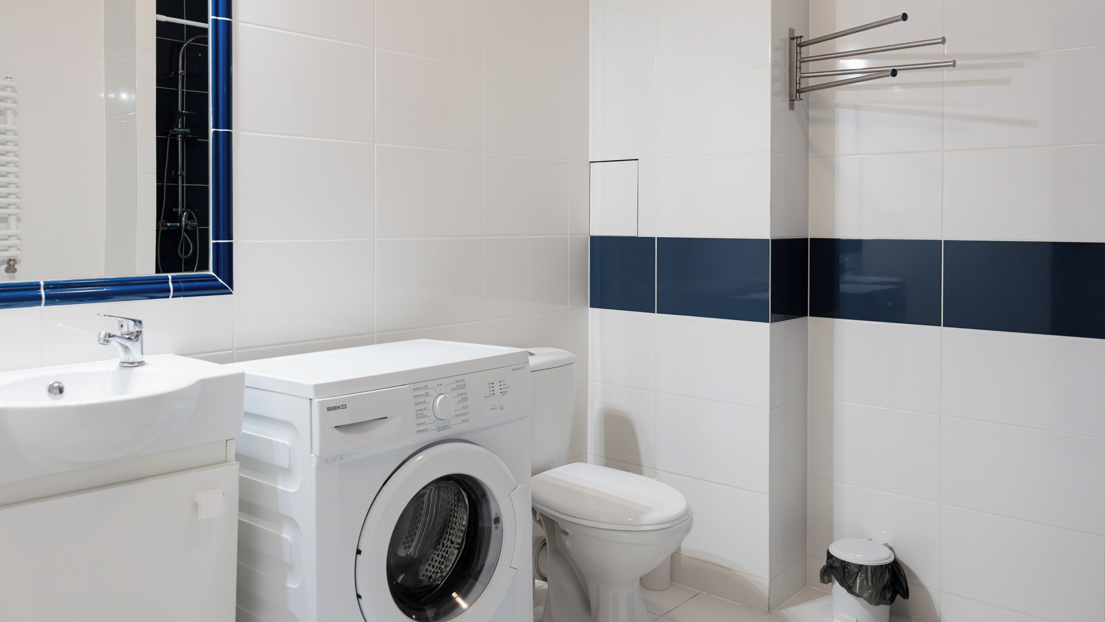 A modern bathroom with a washing machine, toilet, sink, and a towel rack.