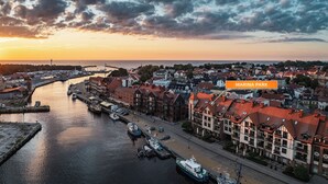 A marina with boats docked, a waterfront promenade, and traditional buildings.