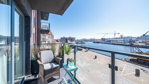 A balcony with wicker furniture, potted plants, and a view of a marina with boats and buildings.