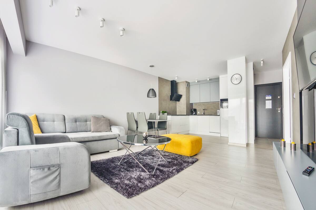 Una sala moderna con un sofá seccional gris, una mesa de centro redonda de vidrio y un taburete amarillo.