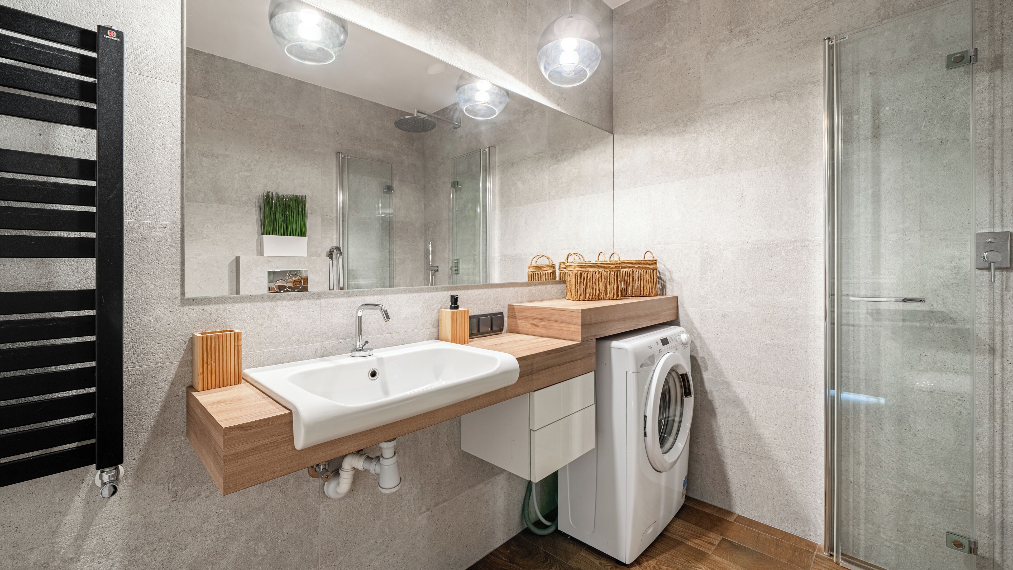 A modern bathroom with a large mirror, a sink, a washing machine, and a glass shower enclosure.