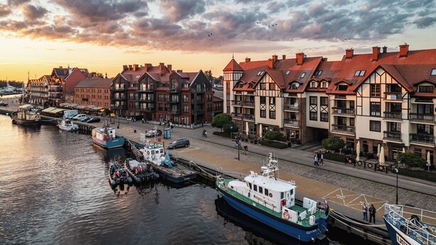 A waterfront with traditional buildings, a dock with boats, and a pedestrian walkway.