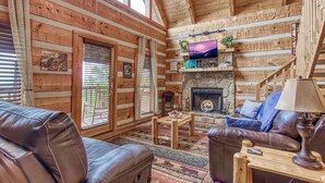 A log cabin interior with a stone fireplace, leather furniture, and a television mounted above it. - View-topia! VIEWS, VIEWS AND MORE VIEWS (Sevierville)