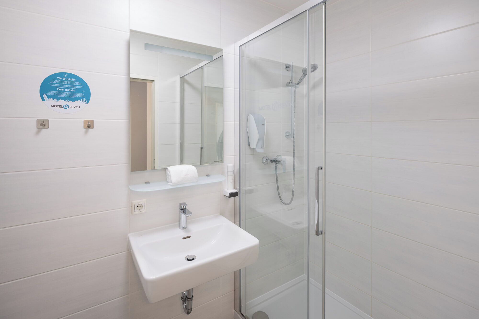 Une salle de bain moderne avec une douche à parois de verre, un lavabo blanc et un miroir au-dessus.