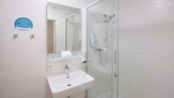 Une salle de bain moderne avec une douche à parois de verre, un lavabo blanc et un miroir au-dessus.