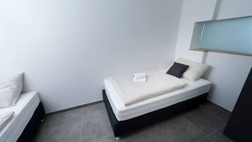 A small, modern bedroom with a single bed, a nightstand, and a built-in shelf above the bed.