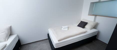 A small, modern bedroom with a single bed, a nightstand, and a built-in shelf above the bed.