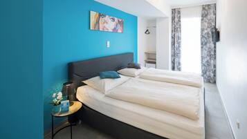 A modern hotel room with a large bed, a small side table, a painting on the wall, and a view of the bathroom.