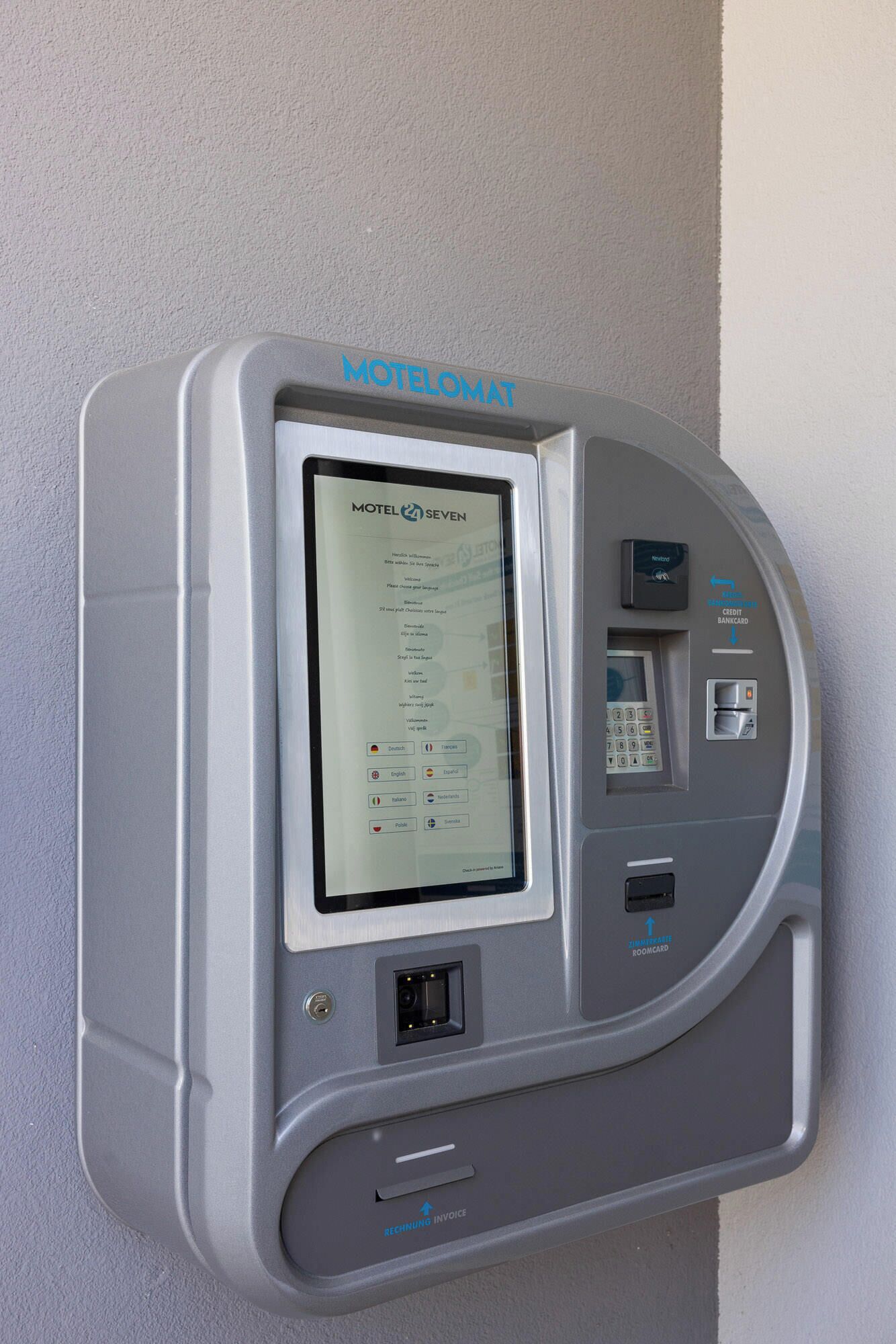 Un quiosco de autoservicio con una pantalla que muestra 'Motel 7 SEVEN' y diversas opciones de pago, incluyendo tarjeta de crédito y tarjeta de habitación.