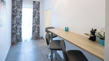 Una habitación de hotel moderna con una mesa de comedor de madera, sillas tapizadas en gris, una pequeña planta en maceta y un cartel que indica una política de no fumar.