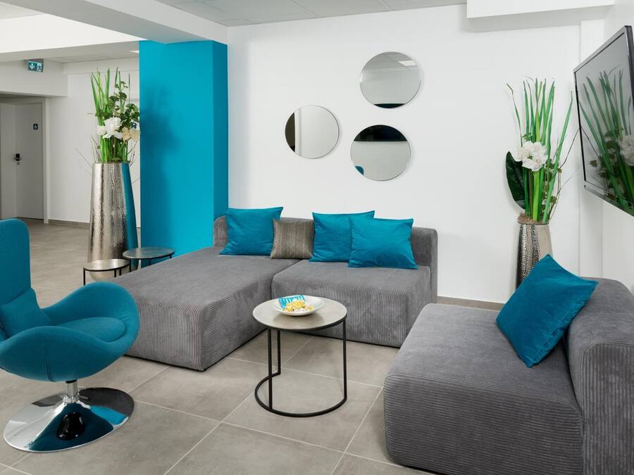 Un área de espera moderna con un sillón azul, sofás grises y una mesita redonda con un bol de aperitivos.