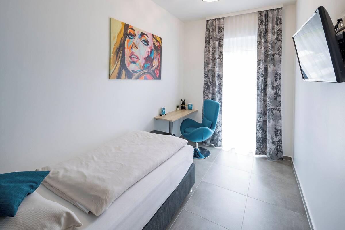 Ein Schlafzimmer mit einem Bett, einem Schreibtisch, einem Stuhl und einem Bild an der Wand.