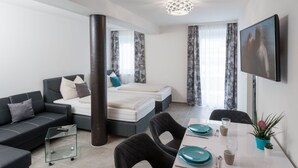 A modern hotel room with a sofa, a bed, a dining table with chairs, a TV, and a large window with curtains. - Motel24seven (Bruck an der Mur)