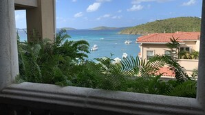 Une vue sur la côte depuis un balcon, avec des bateaux sur l’eau, de la verdure et un bâtiment avec un toit rouge.