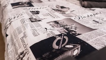 A bed with a newspaper print bedspread, a black headboard, and a folded towel on the side.