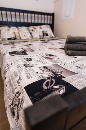 A bed with a newspaper print bedspread, a black headboard, and a folded towel on the side. - Excellent Location - Minutes to the Mountain (North Vancouver)
