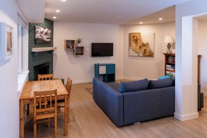 A modern living room with a fireplace, a flat-screen TV, a sofa, and a dining table. - Excellent Location - Minutes to the Mountain (North Vancouver)