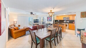 Un salón espacioso con una mesa de comedor de madera, asientos cómodos, un televisor y una zona de cocina con electrodomésticos modernos.