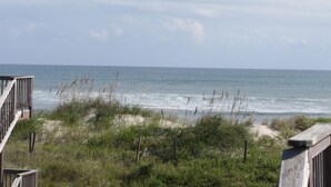 Uitzicht op een strand met een houten terras en weelderige begroeiing.