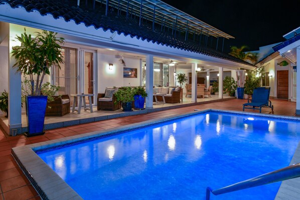 Une piscine dotée d’une terrasse carrelée, entourée d’espaces de détente en plein air et de plantes en pot.