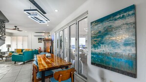 A spacious dining area with a wooden table and chairs, a teal sofa, and a large abstract painting on the wall. - Luxury pool villa totally private backyard - 5 minutes to the beach! (Noord)