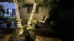 A patio area with a wooden deck, potted plants, and a white chair. - Luxury pool villa totally private backyard - 5 minutes to the beach! (Noord)