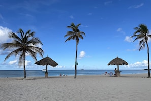 Une plage bordée de palmiers, un parasol en feuilles de palmier et un poste de surveillance des sauveteurs.