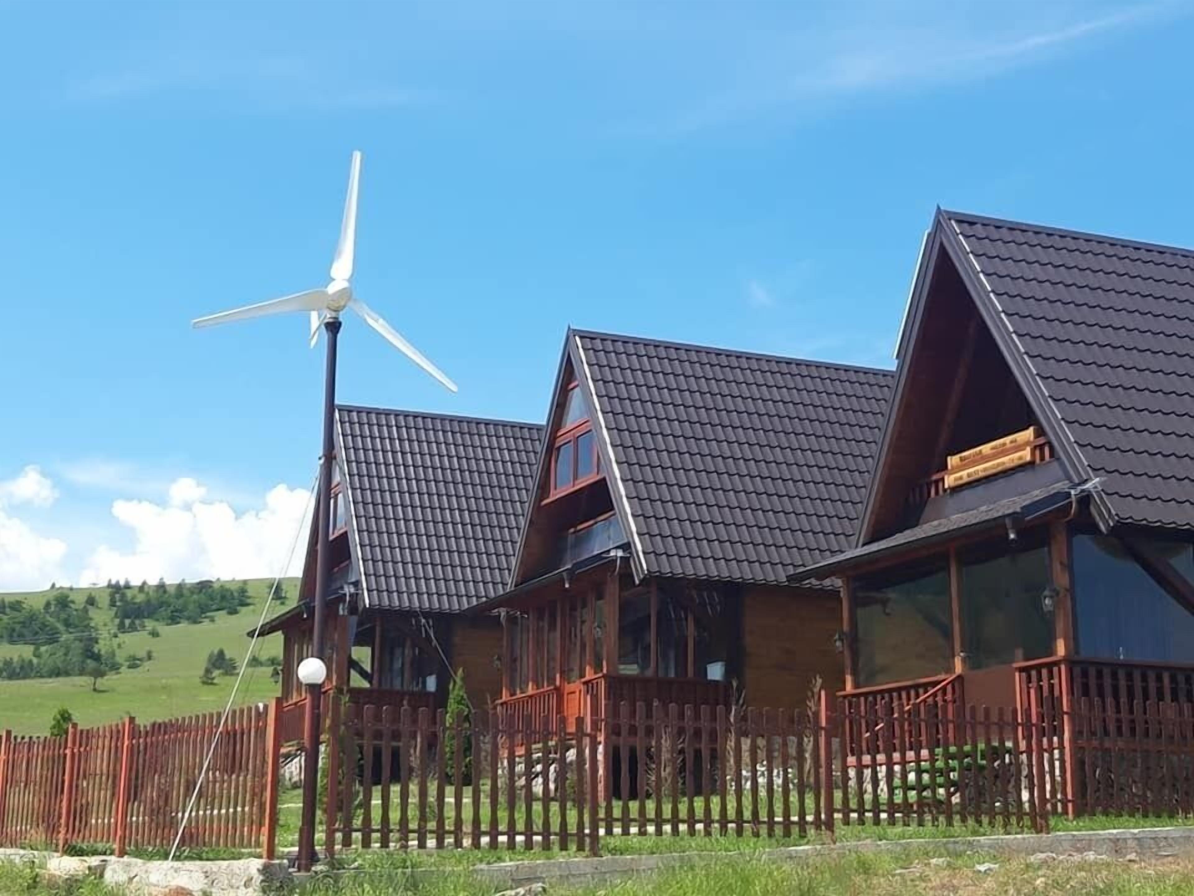 Une cabane en bois avec un toit en pente, une éolienne et une clôture en bois.