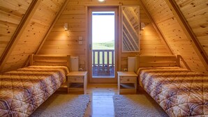 Ein gemütliches Schlafzimmer im Dachgeschoss mit zwei Betten, einer Holztür und Blick ins Freie.
